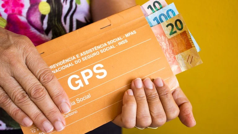 Pessoa segurando guia GPS do INSS com cédulas de real visíveis, representando contribuição previdenciária e pagamento ao INSS 2 vezes por ano.