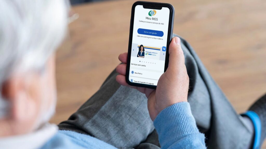 Idoso acessando o aplicativo Meu INSS no celular para consultar informações sobre benefício previdenciário e pente fino do INSS.
