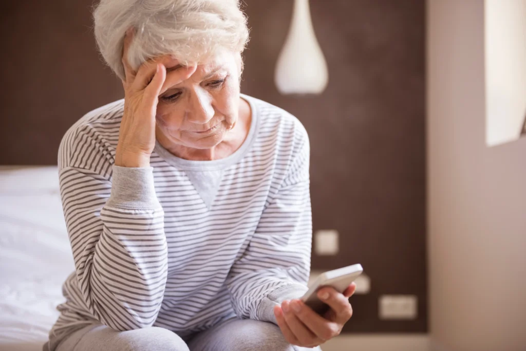 Mulher idosa consulta o celular após identificar aposentadoria cessada pelo INSS.