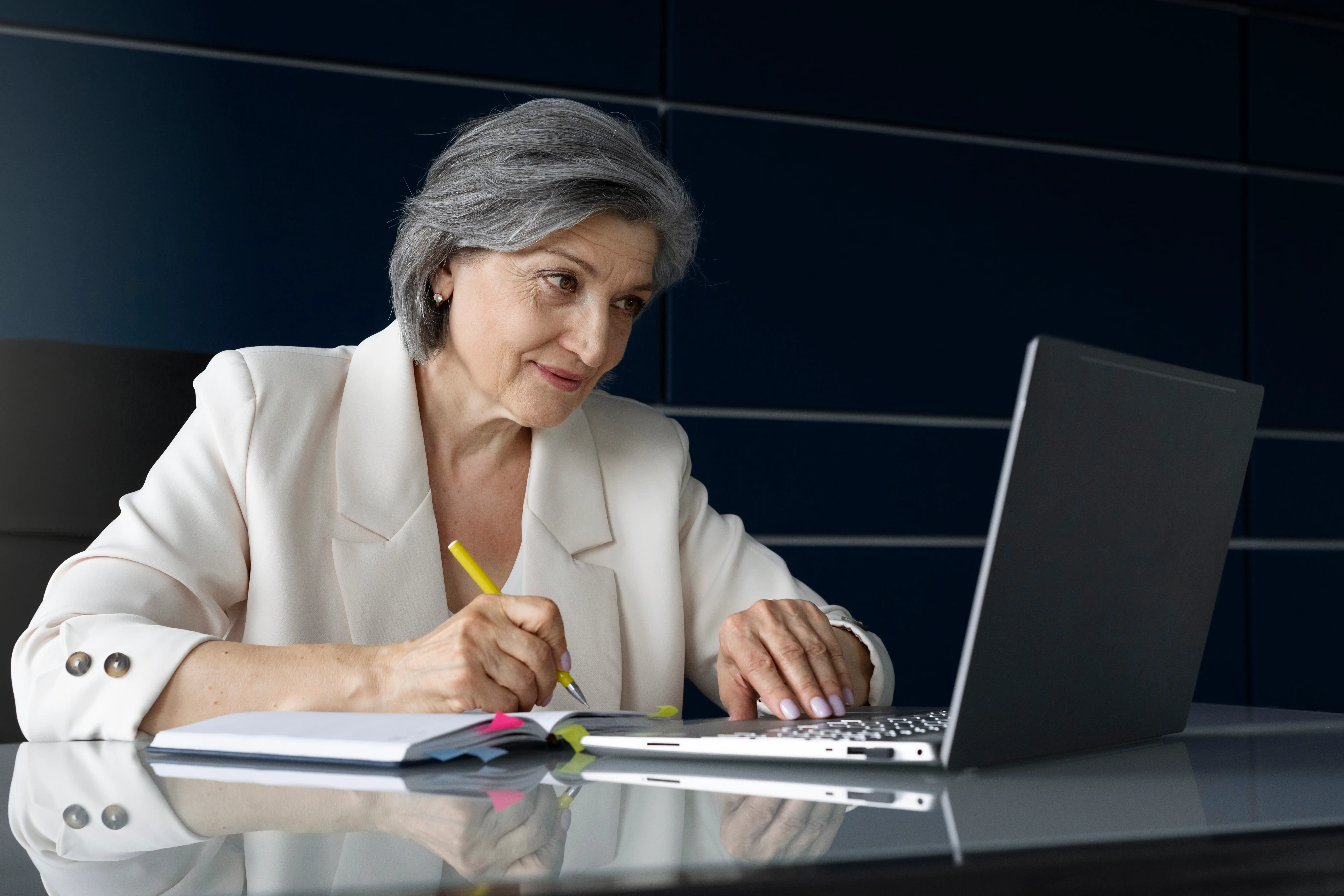 Mulher empreendedora consulta informações sobre aposentadoria do MEI em notebook enquanto faz anotações.